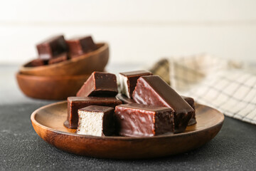 Wooden plate with tasty bird's milk candies on table, closeup