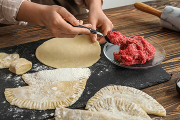 Woman taking spoon of mince while preparing cheburek at table near light wall, closeup