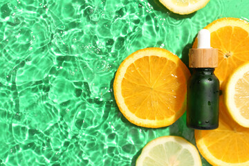 Bottle with vitamin C serum and citrus fruits in water on color background
