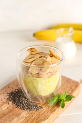 Wooden board with glass of tasty chia seed pudding and banana on light table