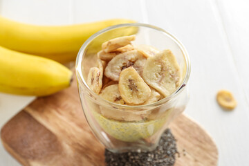 Wooden board with glass of tasty chia seed pudding and banana on light table, closeup