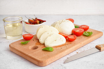 Wooden board with tasty mozzarella cheese and tomatoes on light background