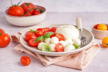 Plate with delicious mozzarella cheese, basil and tomatoes on light background