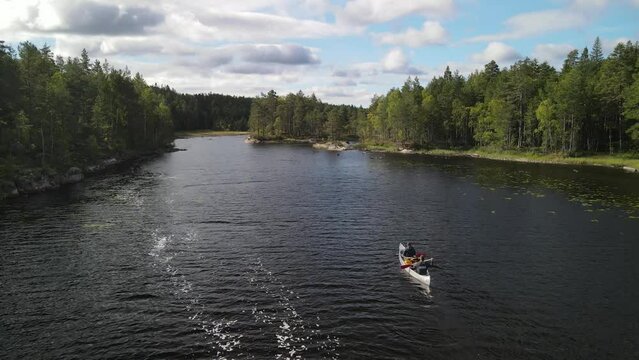 Aerial view of drone flying over Canoers paddling between green pine forest groves on a Swedish lake in Glaskogen nature reserve. Sunny Blue Sky with Clouds with landscape in Sweden