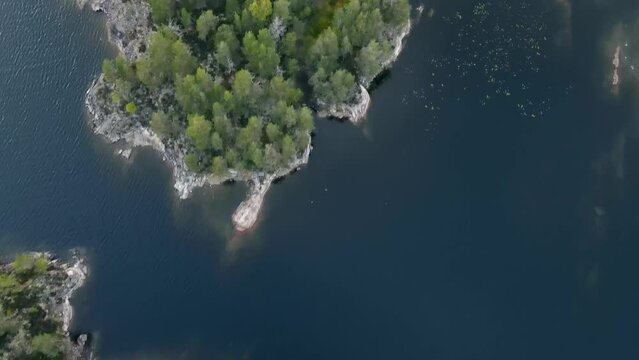 Birds eye view of the Scandinavian Archipelago in Glaskogen, Northern Europe. Drone slowly flies over water and islands filled with rocks and green trees.