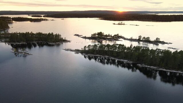 Aerial view of Swedish nature landscape during orange sunset with a clear sky. Drone flies down trough beautiful small islands, Glaskogen