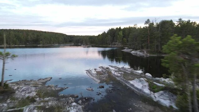 Aerial view flying through trees on a small rocky island surrounded by water. With vast green pine forests and a bright sky in the background, Glaskogens naturreservat