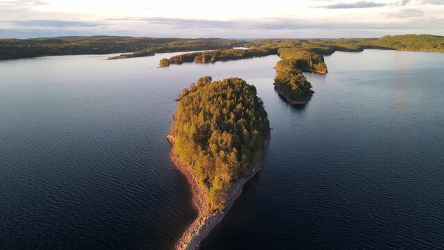 Archipelago in Scandinavia, Northern Europe. Summer day with orange light from beautiful sunset falling over the green pine trees. aerial flying over water and stone islands