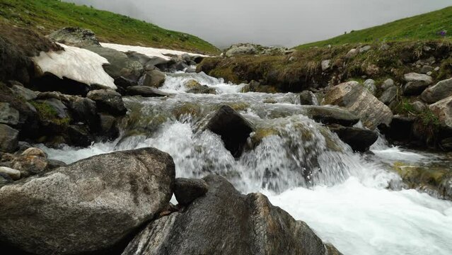 A clear stream runs over stone boulders in the mountains. Water flowing on a rocky stream bed. Wet rocks in the foreground. Behind in the background of the mountain in the fog