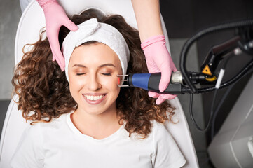 Top view of smiling woman with closed eyes receiving facial skincare treatment in beauty salon....