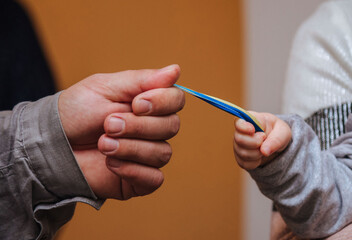 a child's hand and an adult's hand hold a yellow-blue ribbon