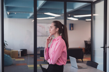 Fototapeta premium Portrait of young smiling business woman in creative open space coworking startup office. Successful businesswoman standing in office with copyspace. Coworkers working in background.