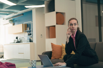 Busy businesswoman using a smartphone. Happy young businesswoman alone in a modern coworking open space office workplace. Business woman connecting with her clients in an office. 