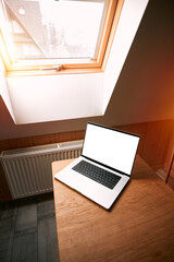 Concept of working remotely and  using laptop indoors. Laptop mockup on a wooden table, blank computer screen. Scandinavian interior and rooftop window.