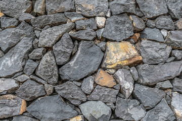 Texture of large black cobblestones of volcanic rock. A wall of large stones of various shapes. Natural background