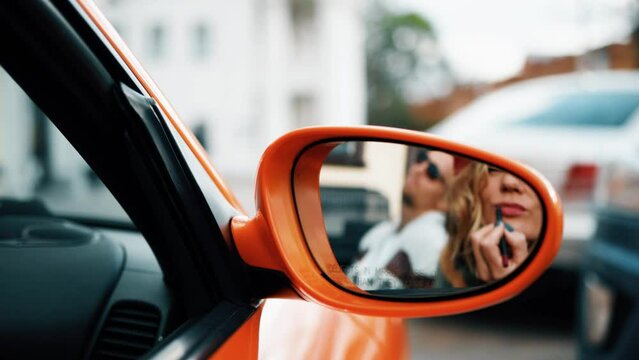 Young adult woman painting lips in car mirror reflection. Female in red beret sitting in orange cabriolet. Autunm and romantic concept.