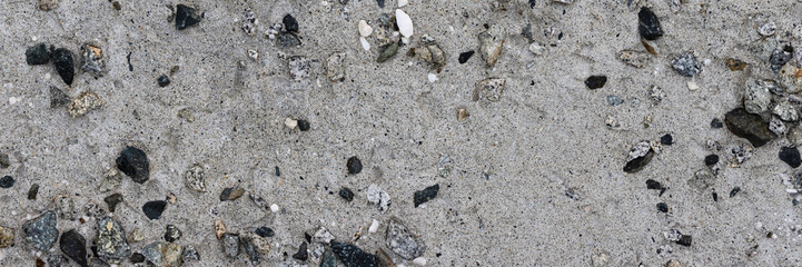 Concrete wall texture with pebbles. Decorative rough concrete surface with white, black and gray stones. Wide panoramic texture for background and design.