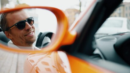 Stylish handsome man in orange cabriolet. Cool reflection in the side view mirror of a car of a male driver. City and autumn consept. - Powered by Adobe