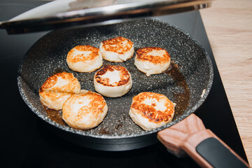 The process of roasting cottage cheese pancake in a frying pan with the lid ajar. Preparing breakfast, selective focus