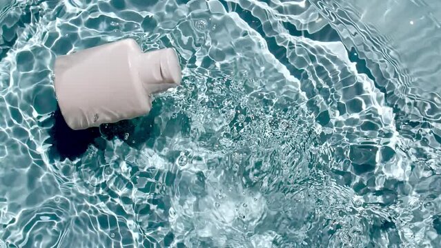 Cosmetic bottle, vial for oil, liquid, collagen serum falling down in water and splashes on blue background. Slow motion. Women's cosmetics skincare. Sample of layout of package beauty product. FullHD