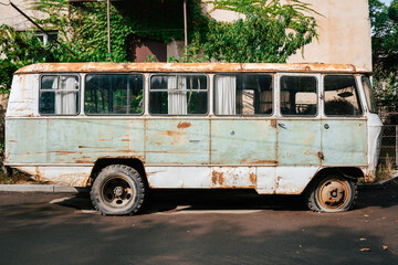 Old, rusty, mint colored Eastern European bus with flat tyres. Lateral view in front of a building with ivy. broken bus