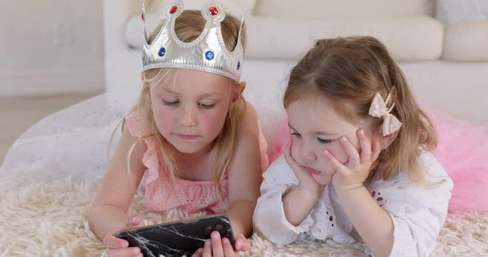 Watching videos, phone and children on floor streaming movies online. Cute, bonding and sisters talk in princess costume using smartphone, internet and technology to play educational games in lounge