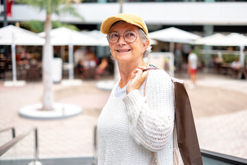 Beautiful senior caucasian woman holding shopping bag as she climbs the escalators in the mall. Happy elderly lady looking around smiling