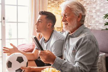 Caucasian couple of young boy and senior grandfather soccer fans watching a football game on tv sitting on a comfortable sofa in living room