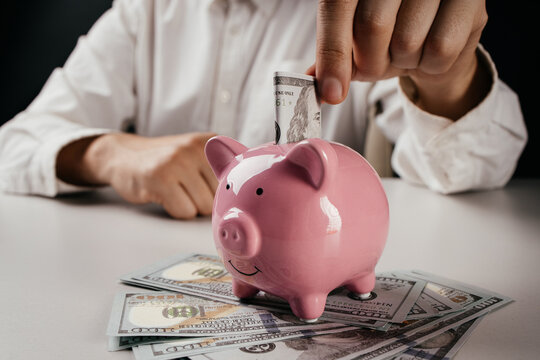 A man is putting dollar bill in a pink piggy bank. Investment or saving money concept