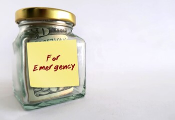 Money jar bottle on copy space white background with yellow stick note written FOR EMERGENCY, means to save cash to use in crisis unexpected life crisis by building emergency fund