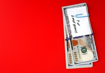 White paper note with text written FOR EMERGENCY  clip with cash dollars money on red copy space background , smart financial planning to save money for contingency fund - for rainy day, future crisis - obrazy, fototapety, plakaty