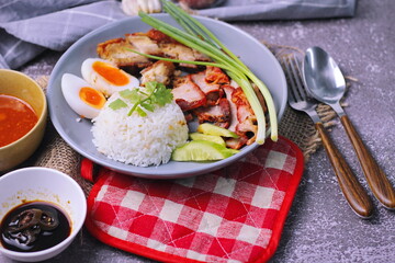 rice with red pork on top served with boiled egg, cucumber and crispy pork with dipping sauce and soy sauce served in the restaurant