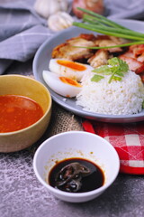 rice with red pork on top served with boiled egg, cucumber and crispy pork with dipping sauce and soy sauce served in the restaurant