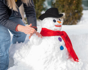 Caucasian woman sculpts a snowman from the snow. The carrot is the place of the nose.