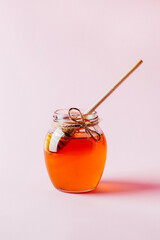 close-up on a jar of honey and a wooden spindle for honey on a pink background