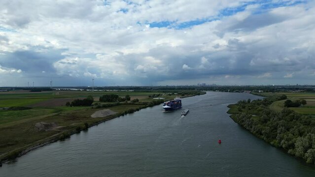 Aerial follow-up shot of freight line container ship BG Onyx sailing across river of Zwijndrecht through vast landscapes and city at far