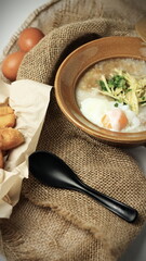 Hot Chinese pork congee top with soft boiled eggs served in a Chinese style clay pot with deep fried dough stick for breakfast. Rice soup concept.
