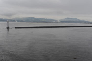 Lighthouse in an ocean bay on a foggy, misty and cloudy grey seascape with horizon at the sea or ocean in Asia