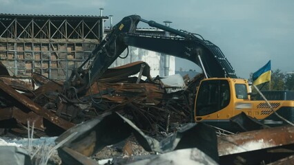 Excavator with Ukrainian flag clearing debris on site of bombed business center. Aftermath of Russian air strikes. Building destroyed by missile attack

