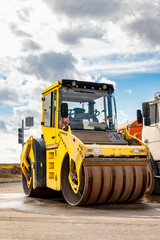 Vibratory road roller lays asphalt on a new road under construction. Close-up of the work of road machinery. Construction work on the construction of urban highways.