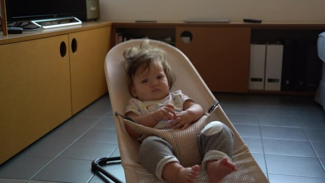 Impatient tired bored baby toddler bouncing up and down chair at home, static