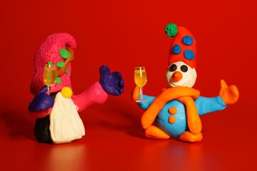 A figure of a dwarf and a snowman made of plasticine with a glass of champagne in his hand on a red background. New Year's Eve. A festive event. Christmas toys.