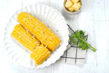 Homemade golden sweet corn cob with butter and cheese on white table