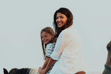 Mother and daughter enjoy riding horses together by the sea. Selective focus 