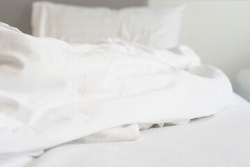 wrinkle messy blanket and white pillow in bedroom after waking up in the morning, from sleeping in a long night, details of duvet and blanket, an unmade bed in hotel bedroom with white blanket