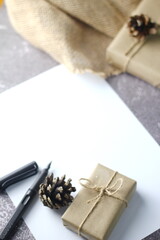 Holidays Gifts. Christmas and New Year..Gift box wrapped in brown paper, pine cones and white paper and pens placed on the table, copy space.