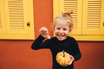 Fototapeta premium Cute little girl holding small pumpkin on the orange background.
