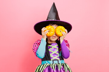 Happy Halloween! young girl with  witch costume and hold  small pumpkins against plain  background