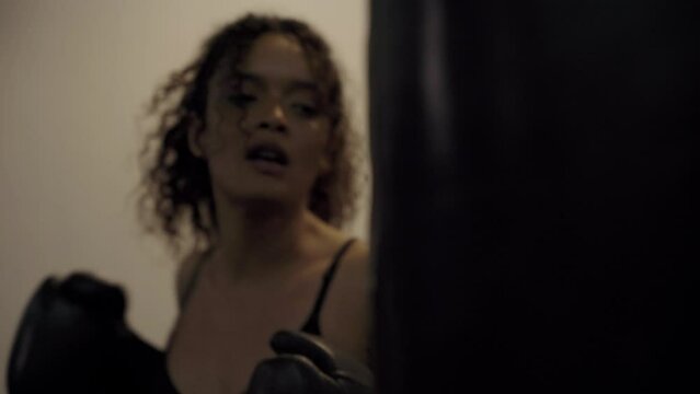 Young biracial woman wearing boxing gloves punching at punching bag at the gym