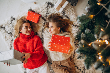Two girls friends lying with christmas presents by the tree